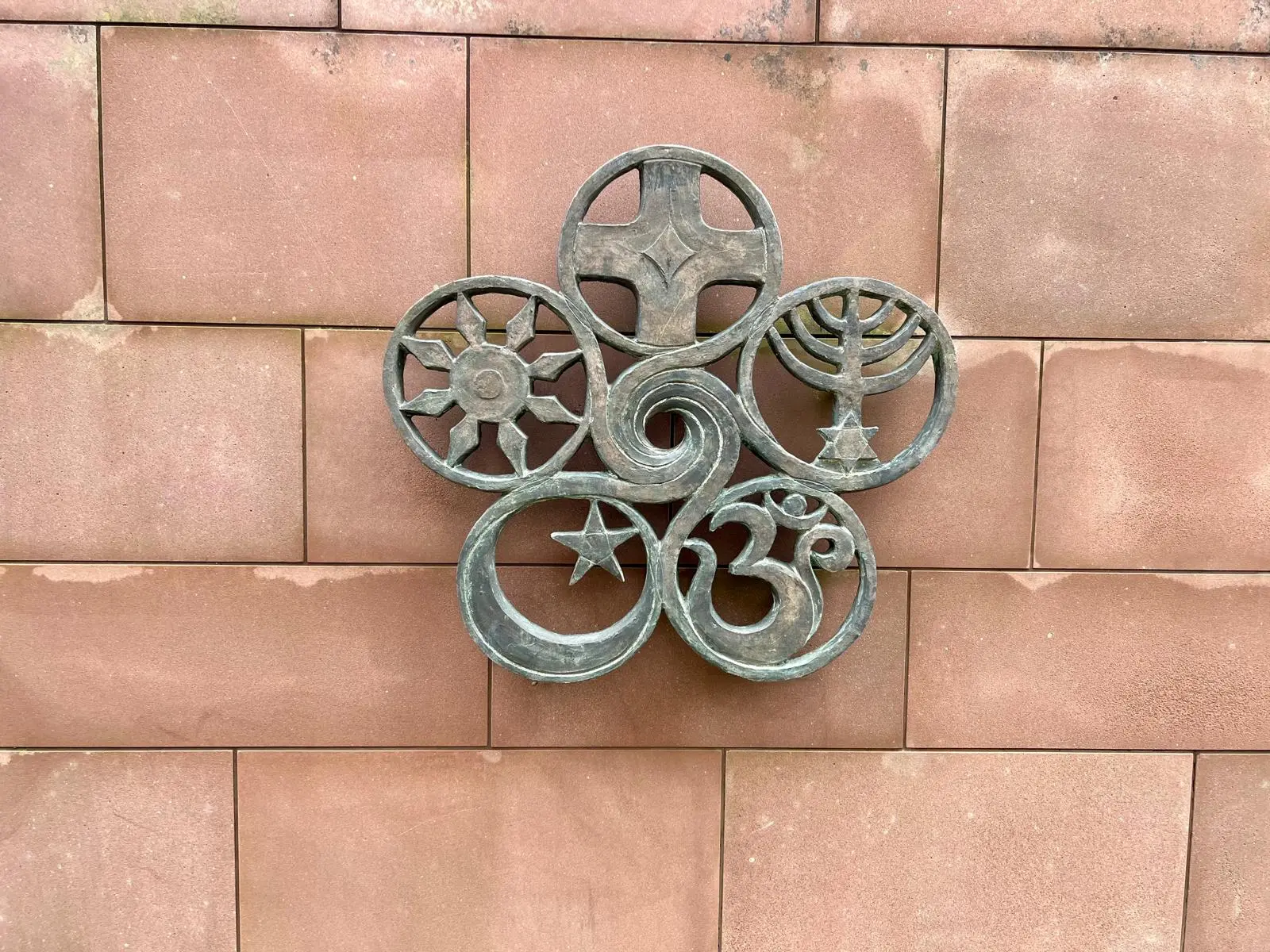 Skulptur mit Symbolen der Weltreligionen an einer Sandsteinmauer