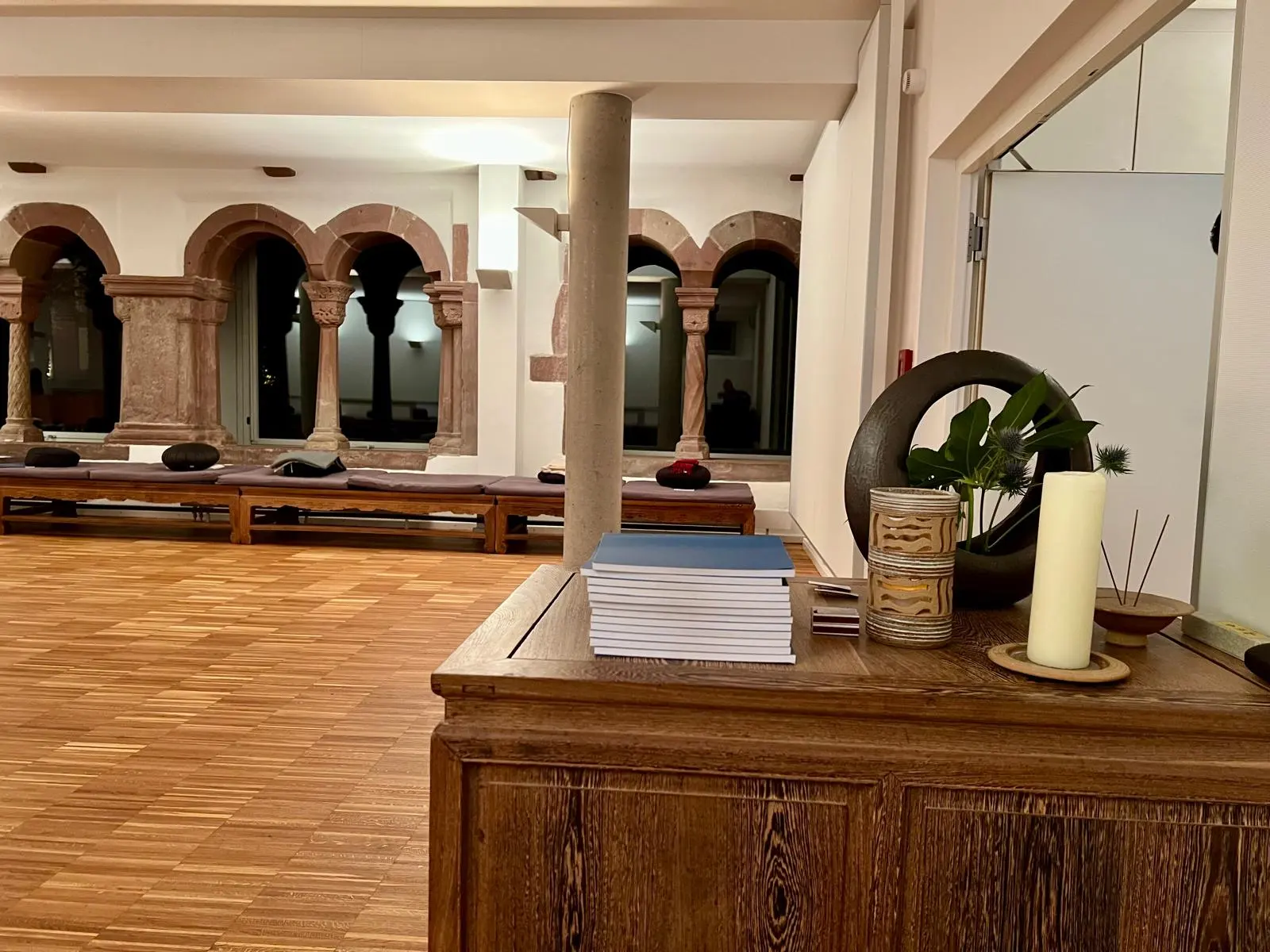 Stiller Meditationsraum mit Holzboden, Kerzenlicht und historischen Bogenfenstern